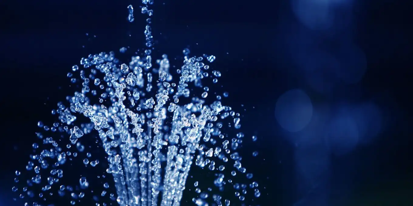 Clean water spraying upward in fine droplets against a dark background