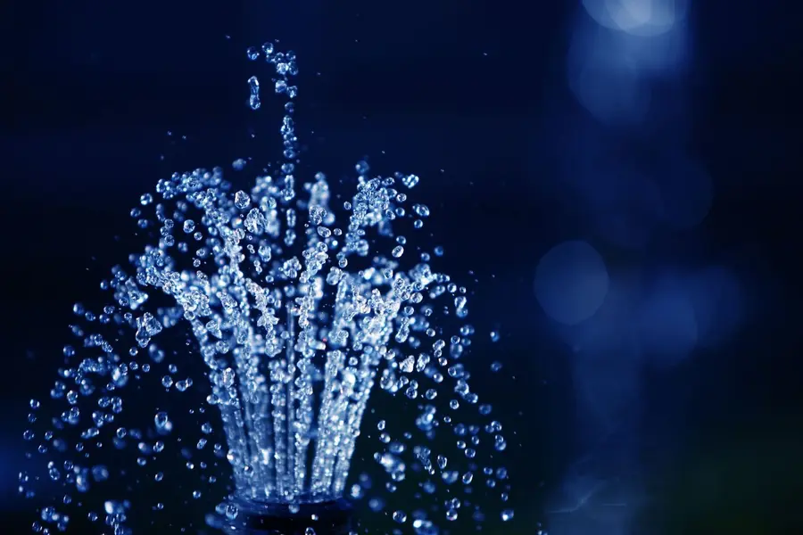 Clean water spraying upward in fine droplets against a dark background