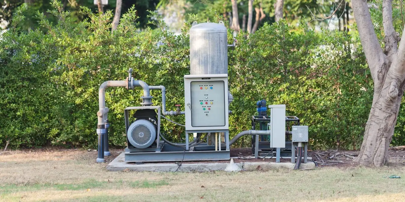 Water well pump station with pressure tank, motor and control panel on a concrete pad