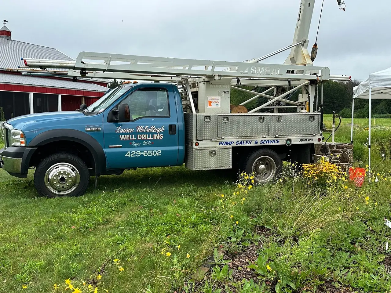 Service truck at a rural job site beside a farm building and canopy